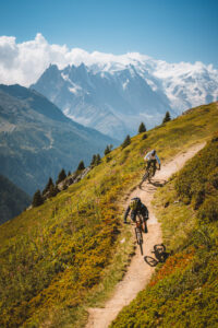 Two mountain bikers riding a singletrack trail with Mont Blanc in the background – photo by Andrea Passerini
